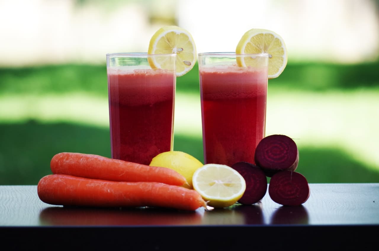 Two delicious fruit and vegetable smoothies on a counter surrounded by carrots and lemons.