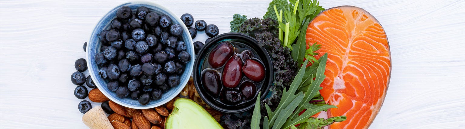 A variety of healthy foods including blueberries, olives, kale, salmon, almonds, and avocado