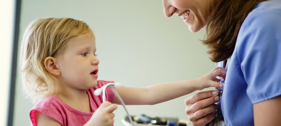 Child playing with a stethoscope and smiling healthcare worker